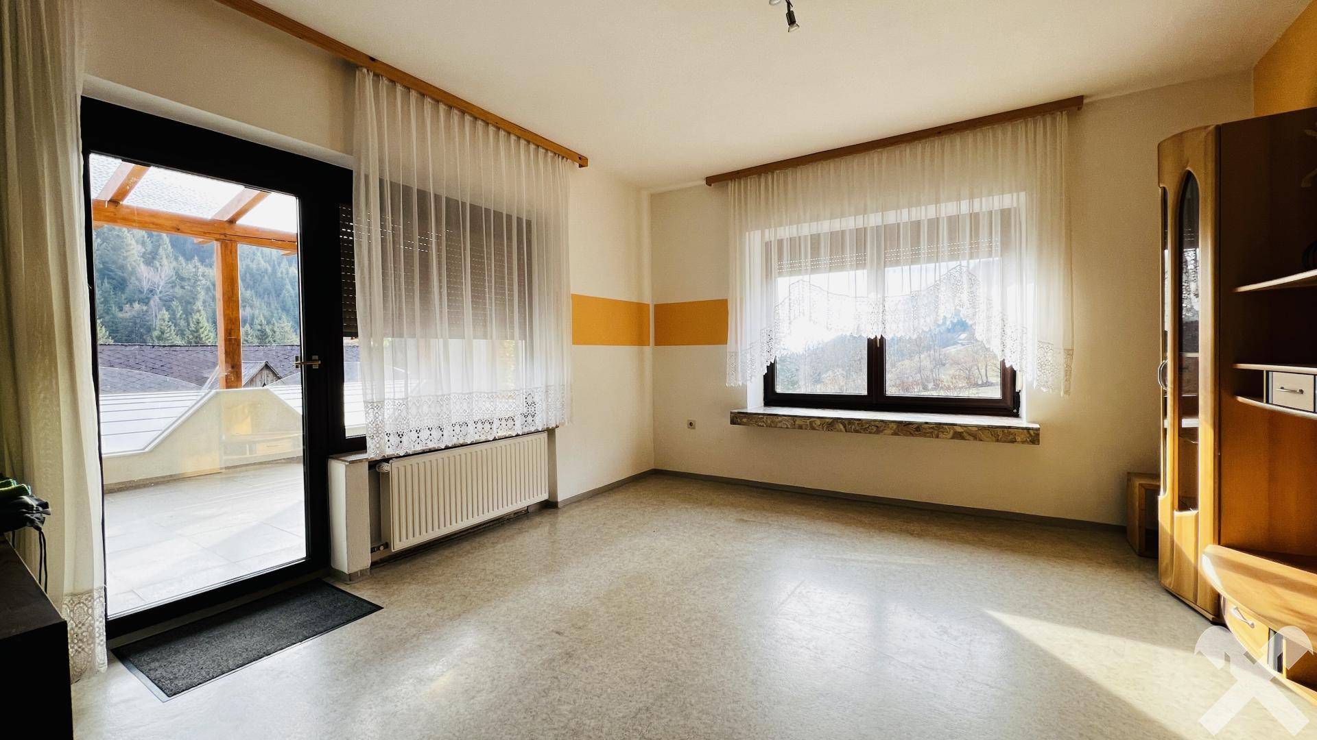 Helles Wohnzimmer mit Zugang zu einer überdachten Terrasse und Blick auf die Berge.