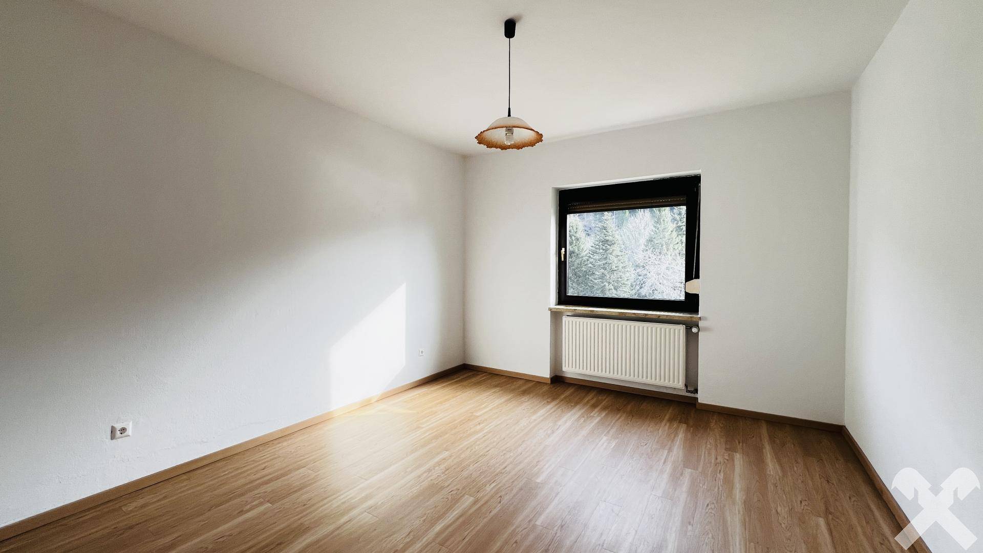 Helles Schlafzimmer mit Holzfußboden und Fenster mit Blick ins Grüne.