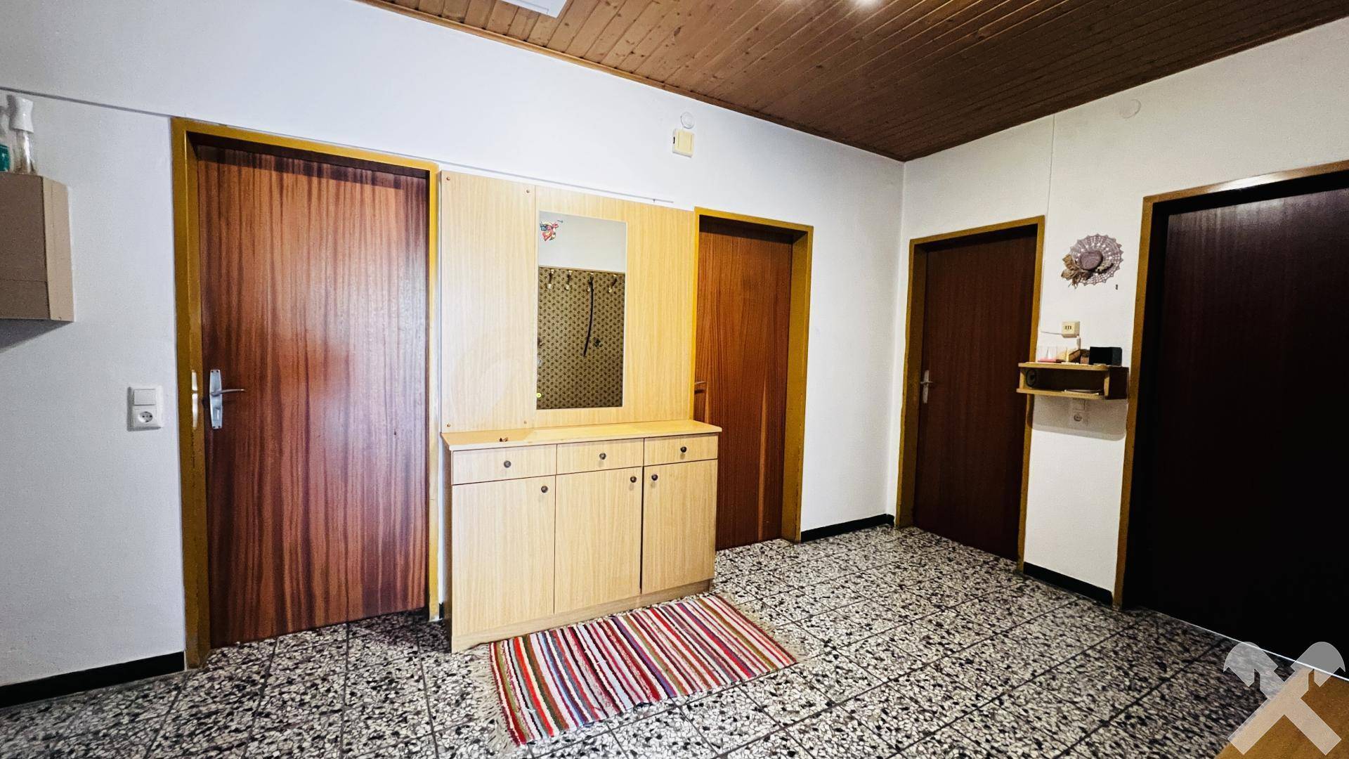 Eingangsbereich mit Garderobe und Fliesenboden, der zu verschiedenen Räumen führt.
