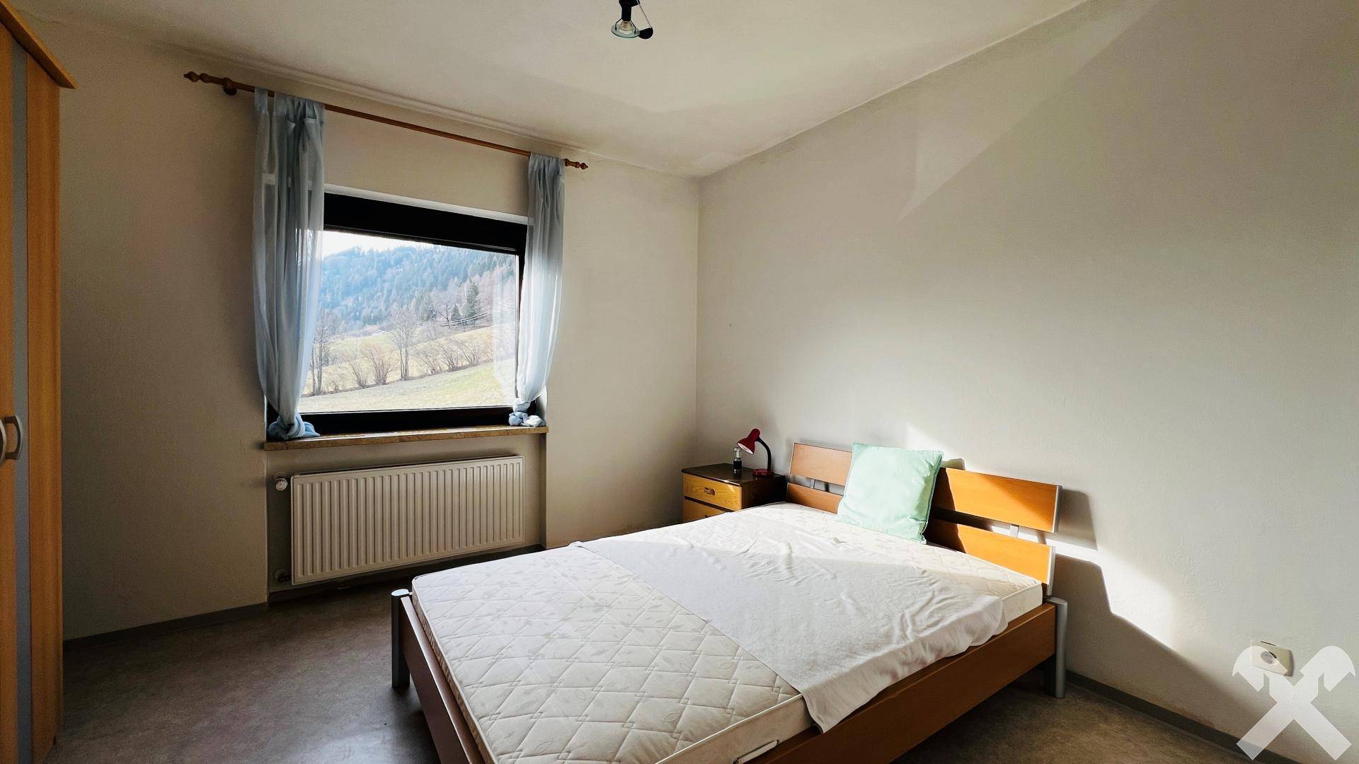 Schlafzimmer mit Doppelbett und Fenster mit Blick auf die grüne Landschaft.