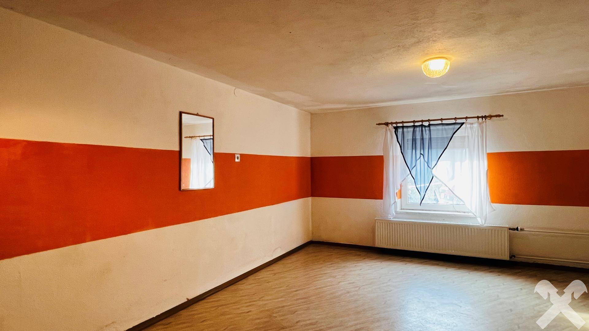 Zimmer mit farbiger Wandgestaltung und Fenster, nutzbar als Schlaf- oder Arbeitszimmer.