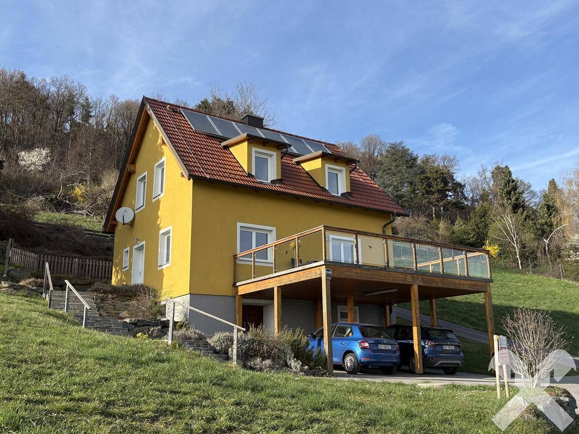 Gelbes Haus mit Satteldach, Photovoltaikanlage und überdachtem Carport auf einem Hanggrundstück.