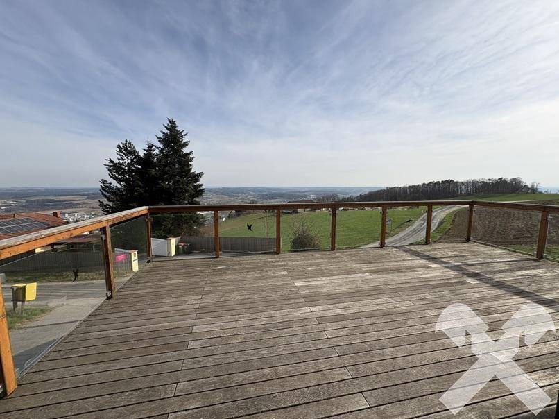 Geräumige Holzterrasse mit Glasgeländer und weitem Blick über die umliegende Landschaft.