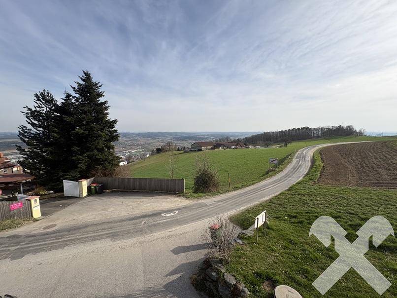 Panoramablick über die weite, grüne Landschaft mit einer Straße und entfernten Siedlungen.