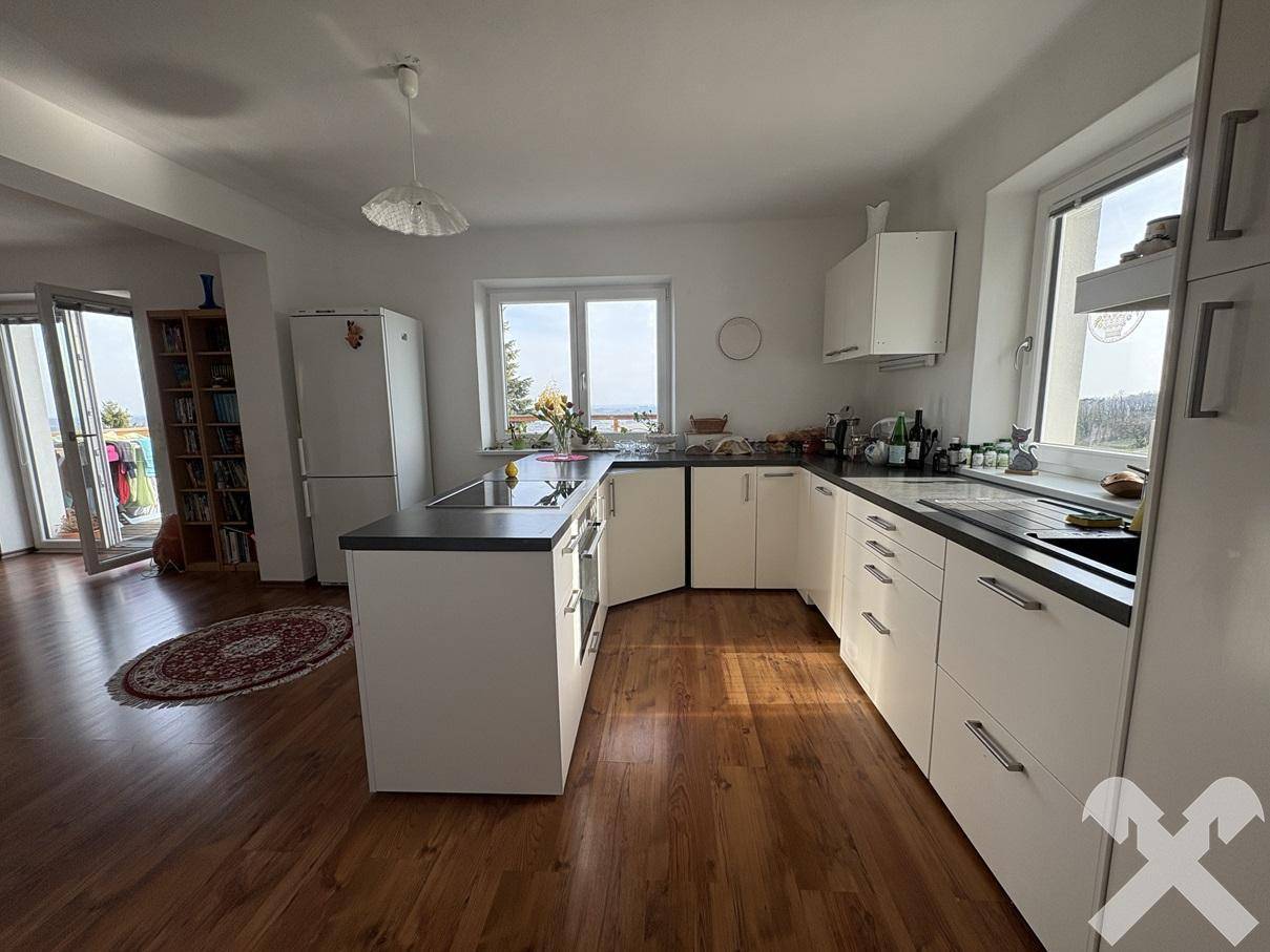 Helle, offene Küche mit weißen Schränken, dunkler Arbeitsplatte und Holzboden, mit Zugang zum Balkon.