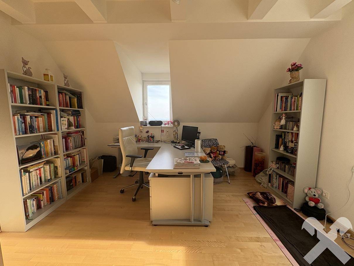 Geräumiges Büro im Dachgeschoss mit Holzboden, Schreibtisch und Bücherregalen, gut beleuchtet.