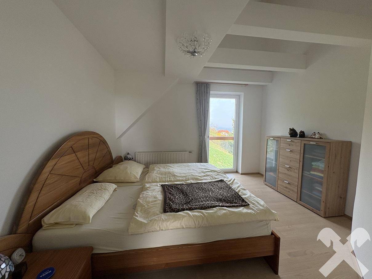 Helles Schlafzimmer mit Holzboden, Doppelbett und Zugang zu einem französischen Balkon.