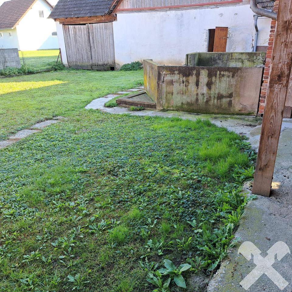 Garten mit Rasenfläche und einer alten Betoneinfassung oder einem Brunnen.