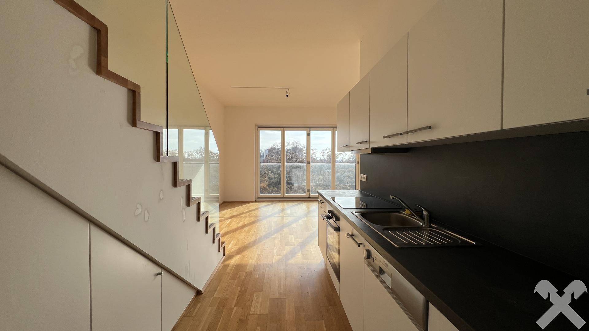 Moderne Einbauküche mit weißen Schränken, dunkler Arbeitsplatte und Blick in den hellen Wohnbereich mit Holzfußboden.