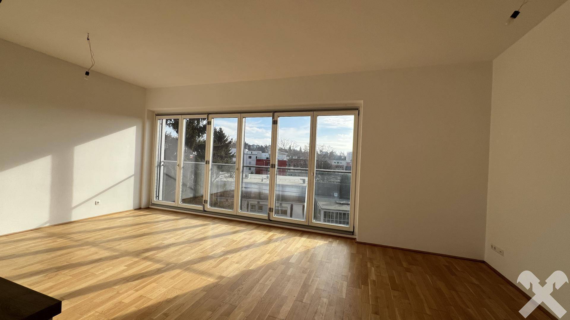 Geräumiger, leerer Wohnbereich mit hellem Holzparkett und großen Falttüren, die viel Tageslicht hereinlassen.