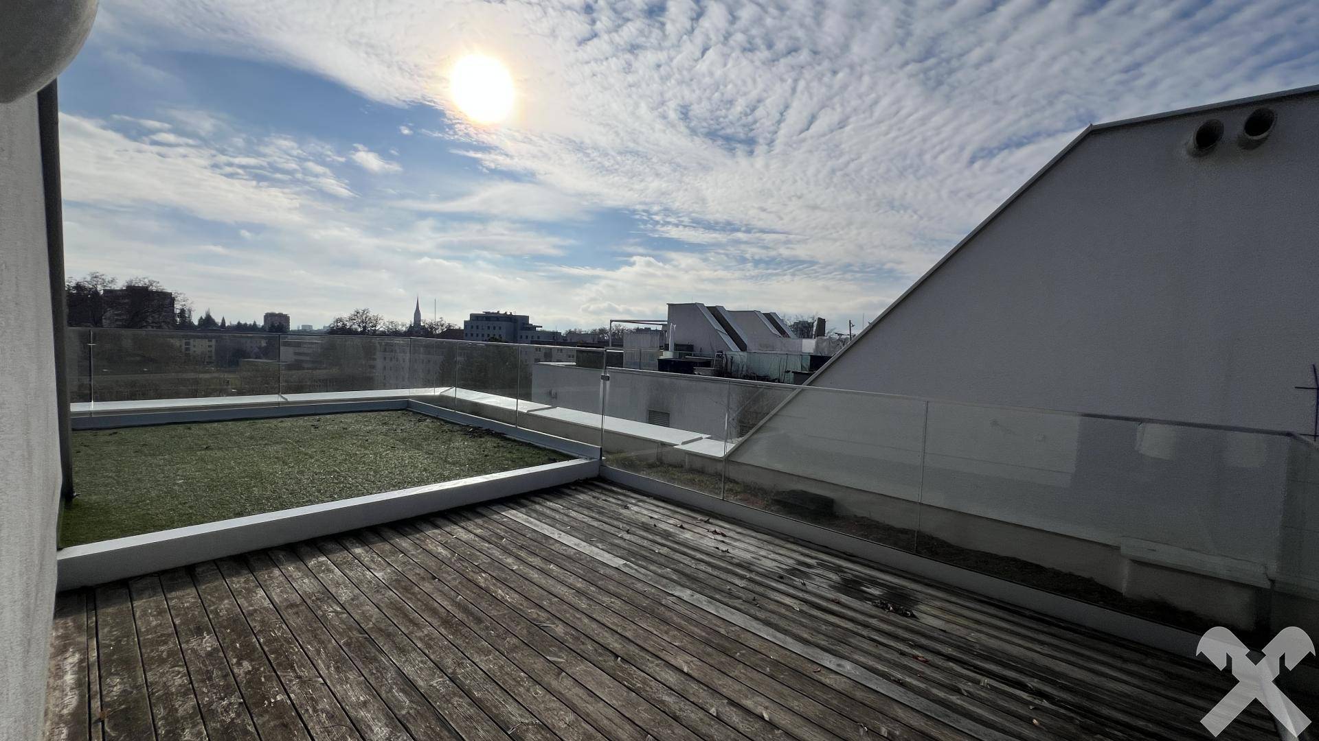 Sonnige Dachterrasse mit Holzbelag, Glasgeländer und Kunstrasenfläche, bietet einen weiten Blick.