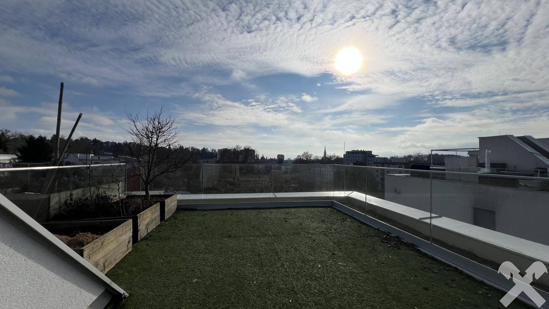 Großzügige Dachterrasse mit Kunstrasen, Pflanzkübeln und Panoramablick über die Stadtlandschaft.