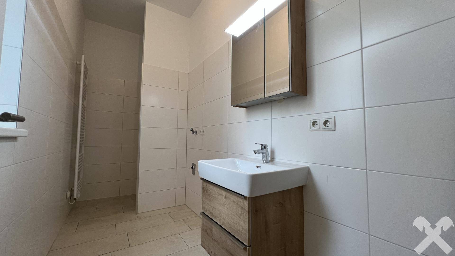 Modernes Badezimmer mit weißen Fliesen, Einzelwaschbecken, Spiegelschrank und begehbarer Dusche.