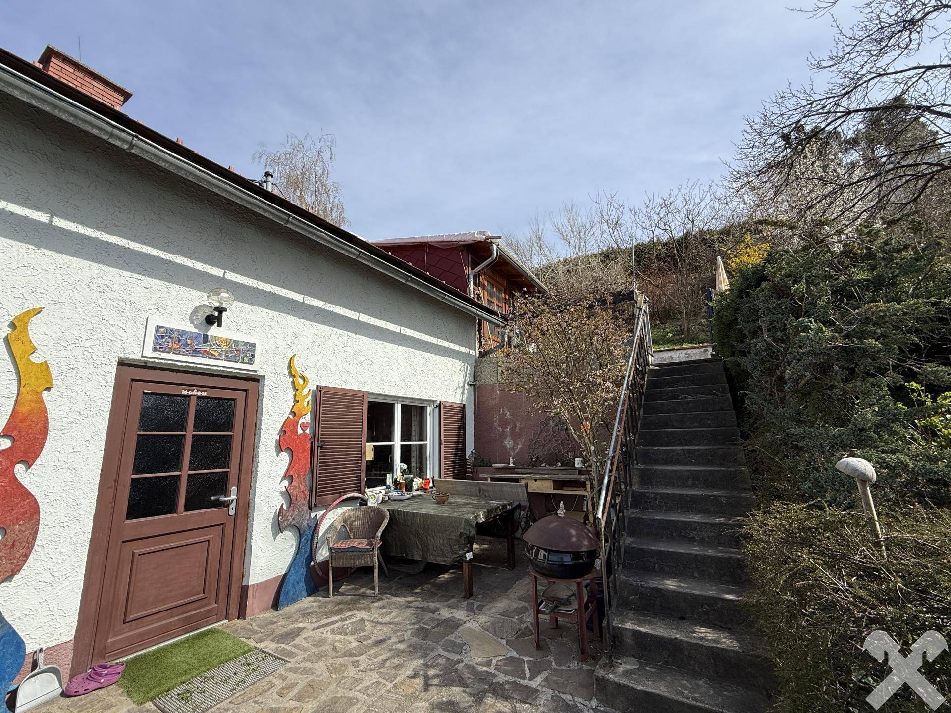Gepflasterte Terrasse mit Esstisch, Stühlen und Grillbereich, ideal für Mahlzeiten im Freien.
