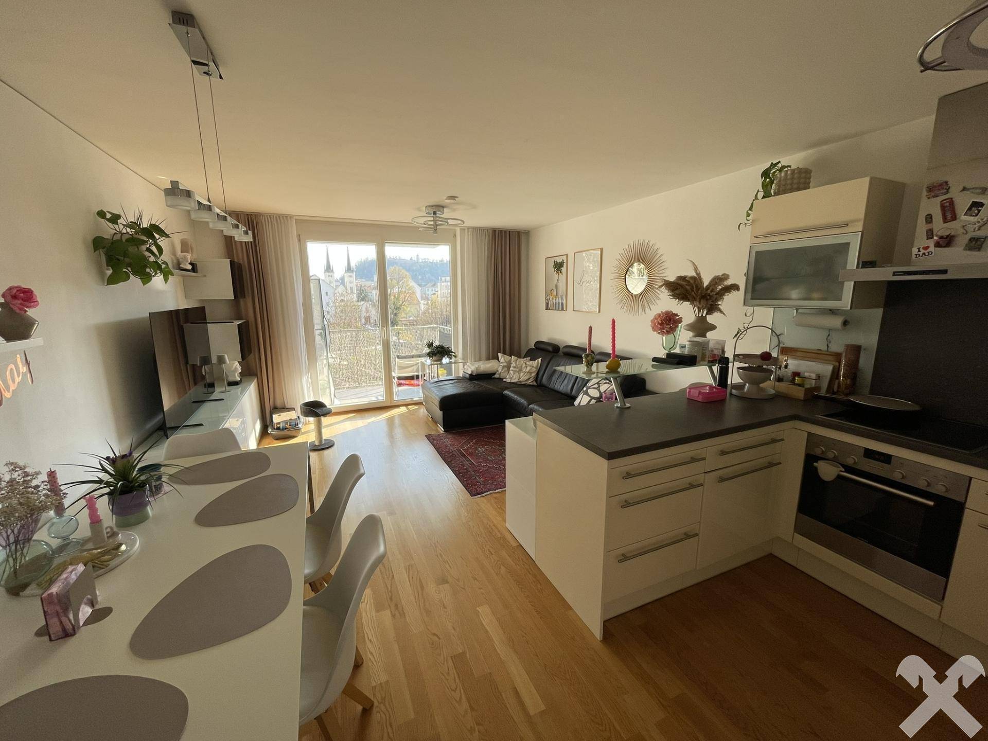 Heller offener Wohn-Essbereich mit integrierter Küche, Holzboden und Zugang zum Balkon.