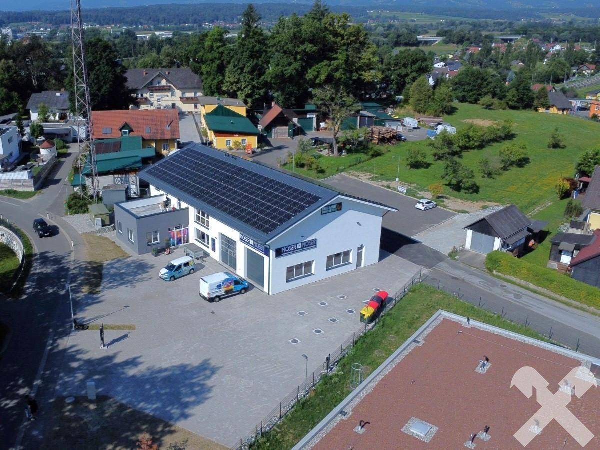 Luftaufnahme des modernen Geschäftsgebäudes mit Photovoltaikanlage auf dem Dach und umliegender Landschaft.