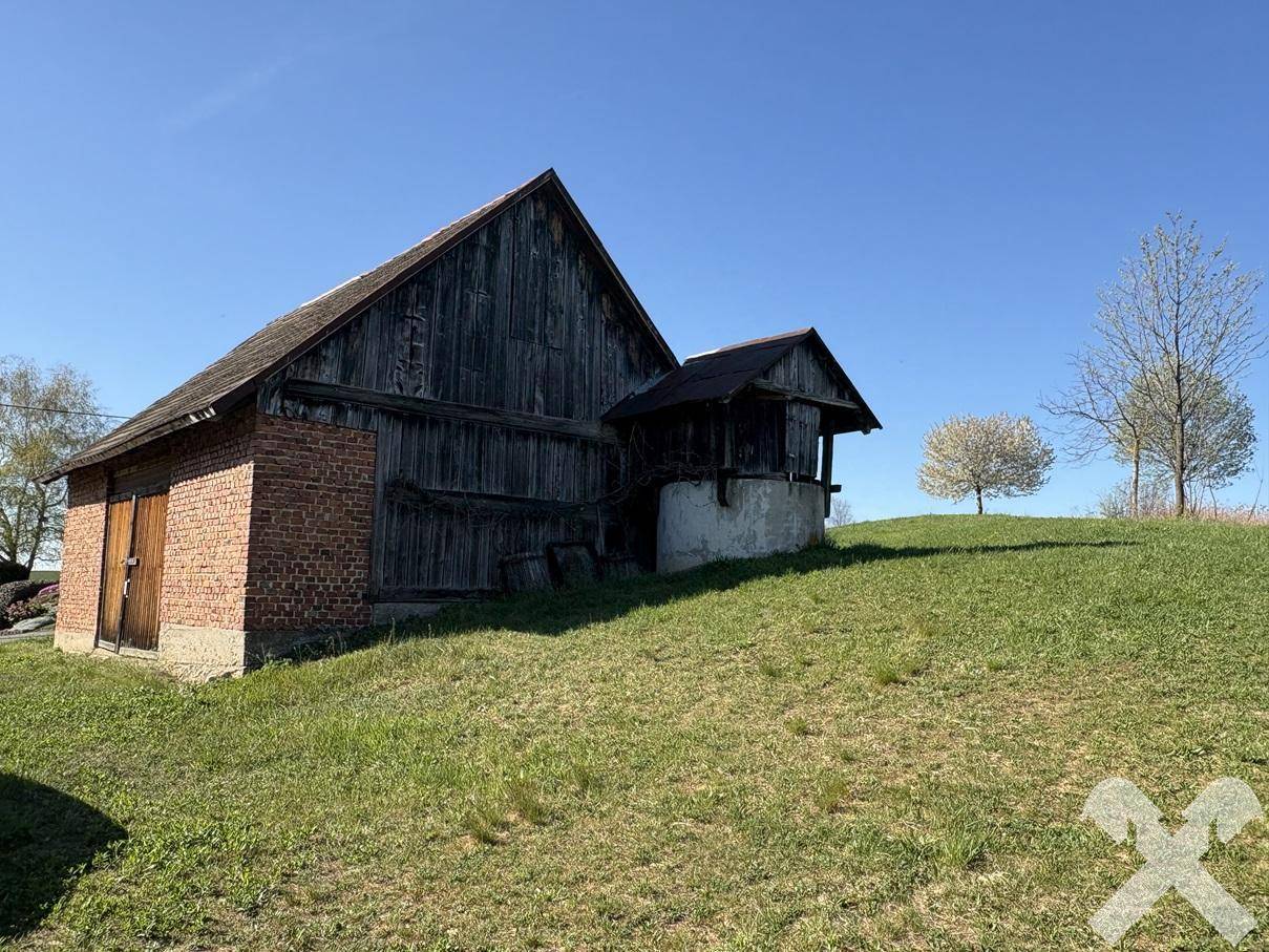 Rustikales Scheunengebäude mit Holzwänden und Backsteinelementen auf einem grasbewachsenen Hügel.