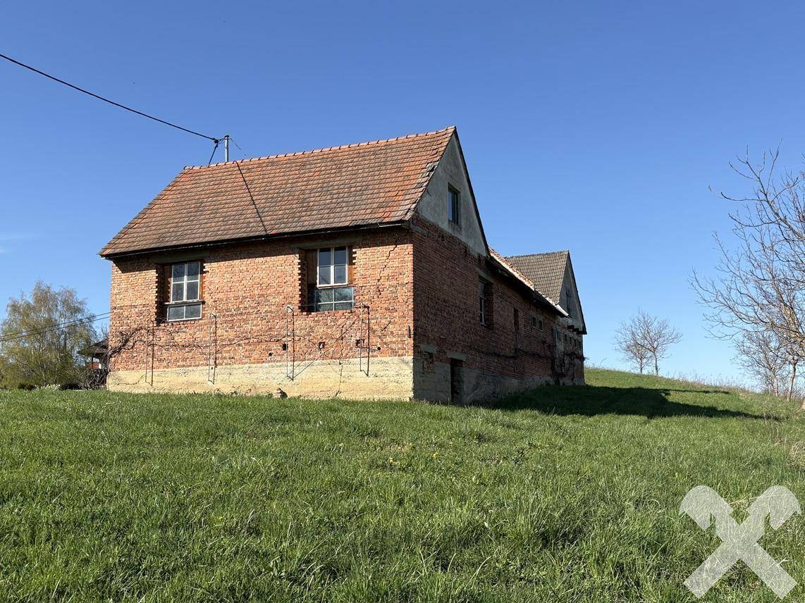 Historisches Backsteingebäude mit Ziegeldach und Fenstern, umgeben von grüner Landschaft.