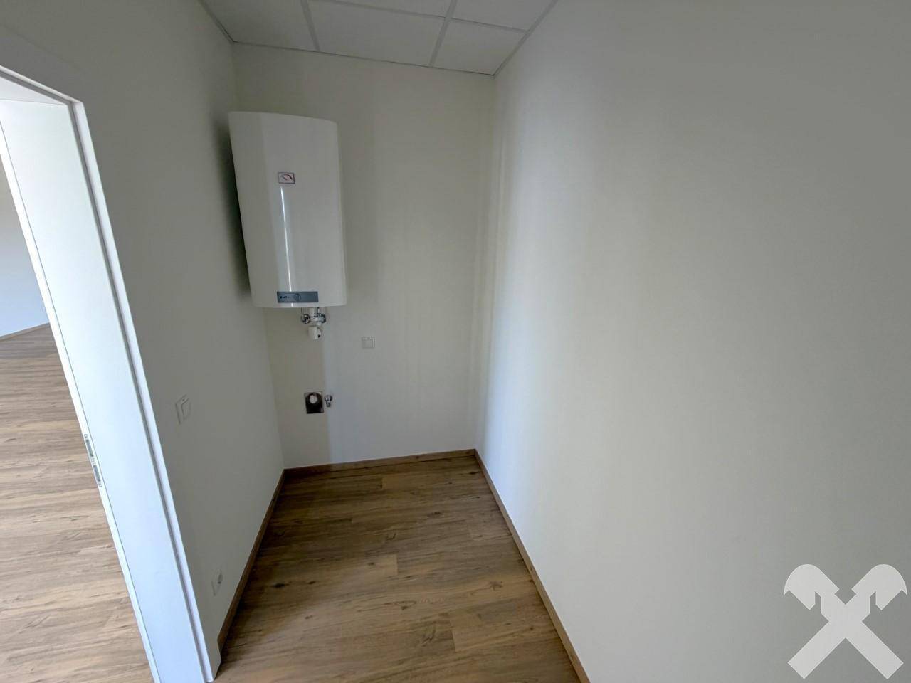 Leerer Raum mit weiß gestrichenen Wänden, Laminatboden und einem Warmwasserbereiter an der Wand.