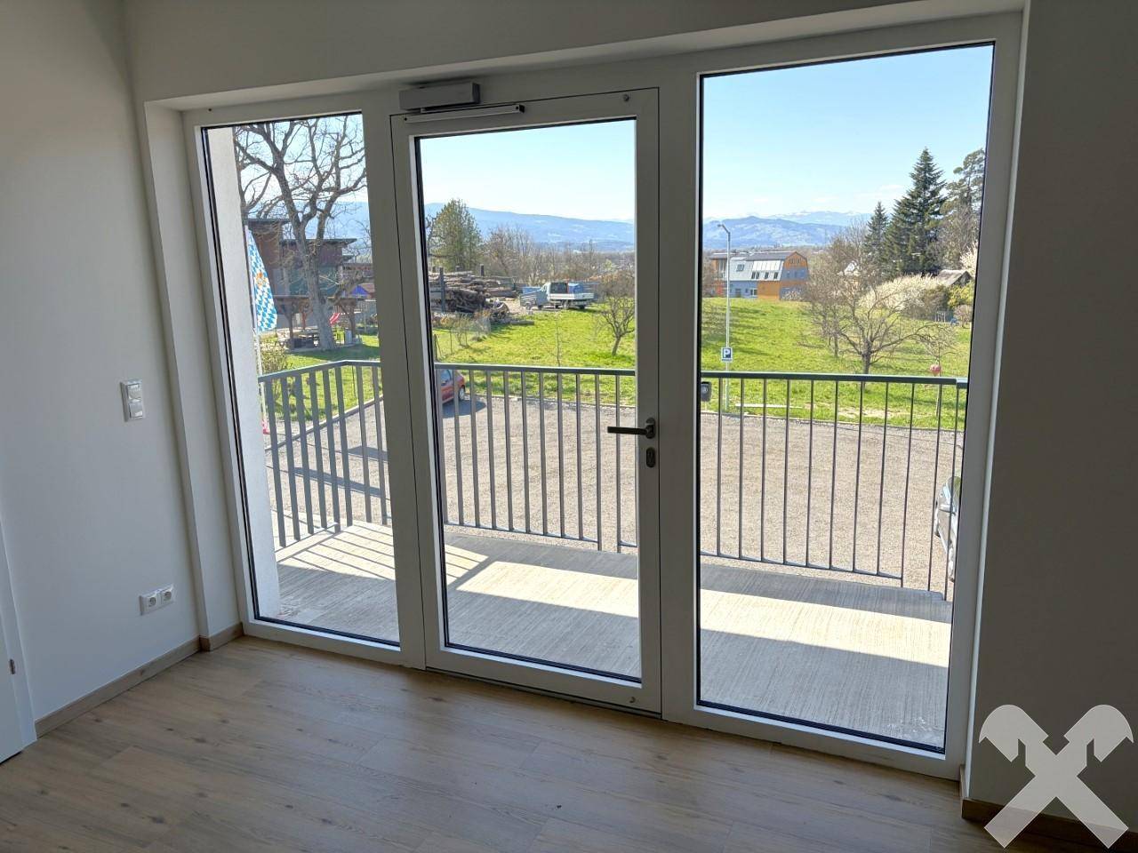 Heller Raum mit großen Fenstertüren, die auf einen Balkon führen und einen weiten Blick ins Grüne bieten.