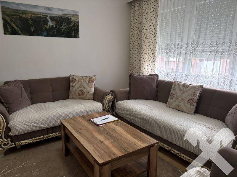 Gemütliches Wohnzimmer mit zwei Sofas, Couchtisch und großen Fenstern mit Vorhängen.