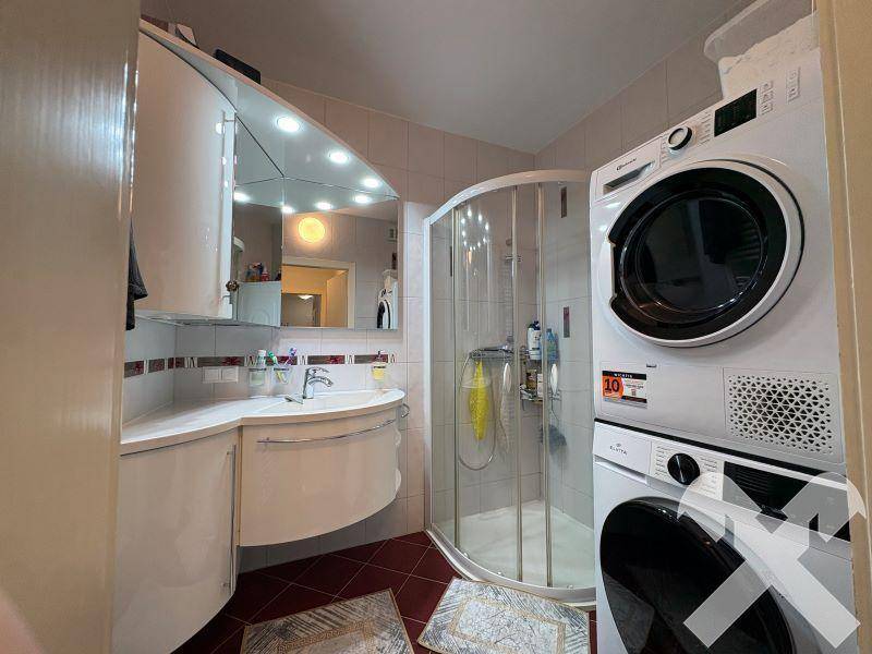 Modernes Badezimmer mit Dusche, Waschbecken, Spiegelschrank und integrierter Waschmaschine.