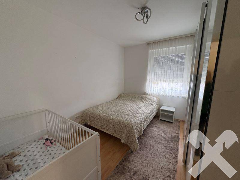 Helles Schlafzimmer mit Doppelbett, Babybett und großem Kleiderschrank mit Teppich.