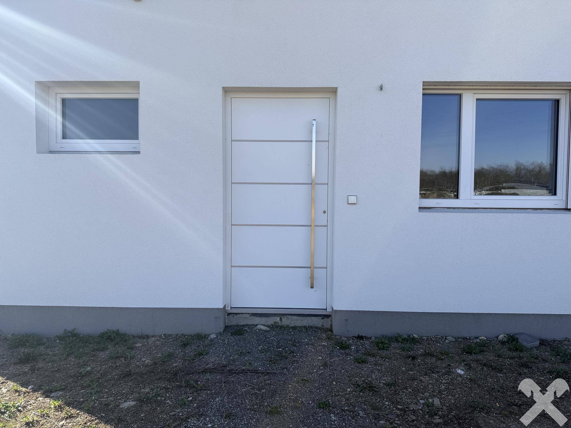 Moderner Hauseingang mit weißer Tür und langem Edelstahlgriff an einer hellen Fassade.