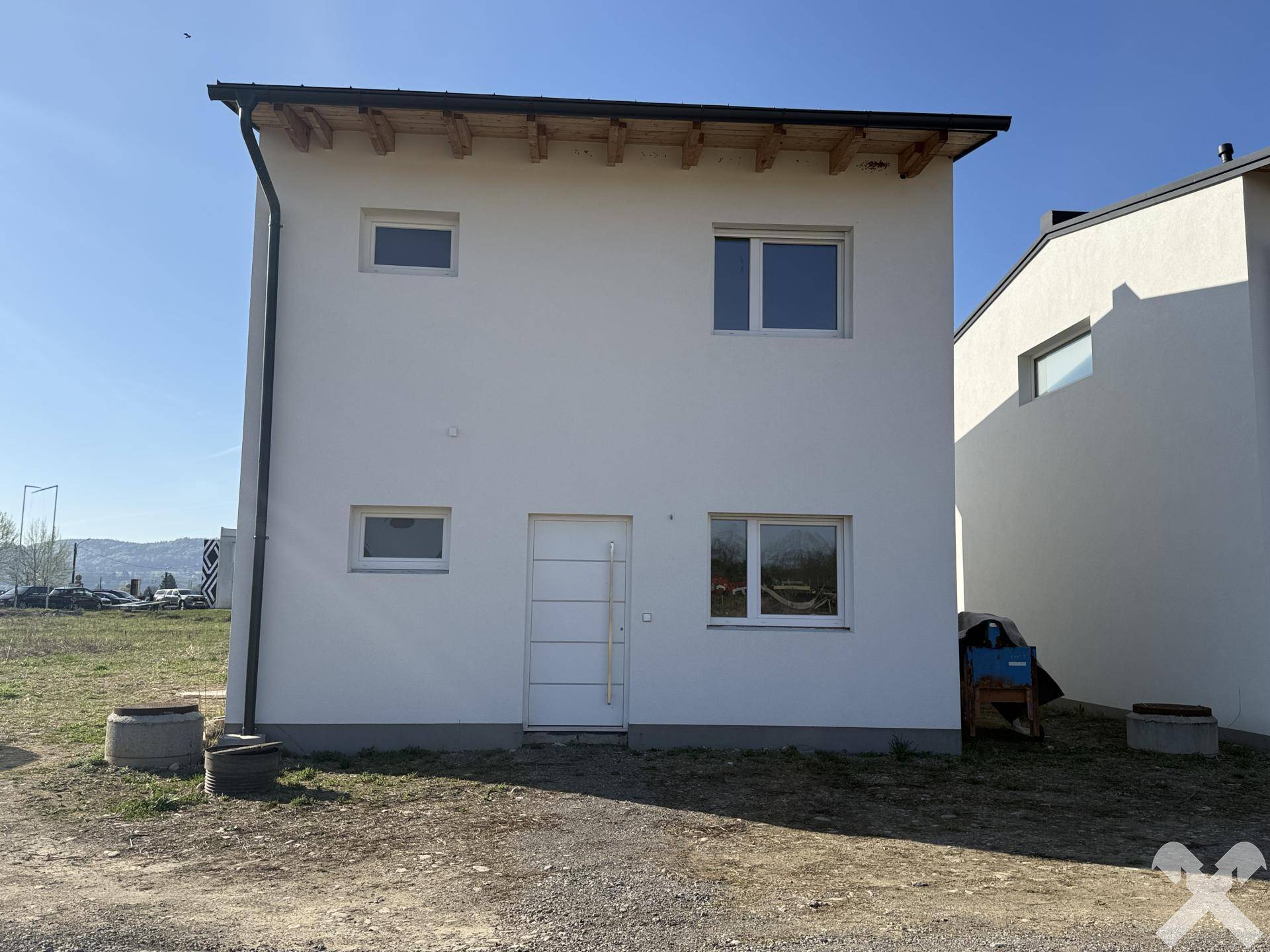 Seitenansicht eines Neubaus mit weißer Fassade und sichtbaren Dachbalken unter blauem Himmel.