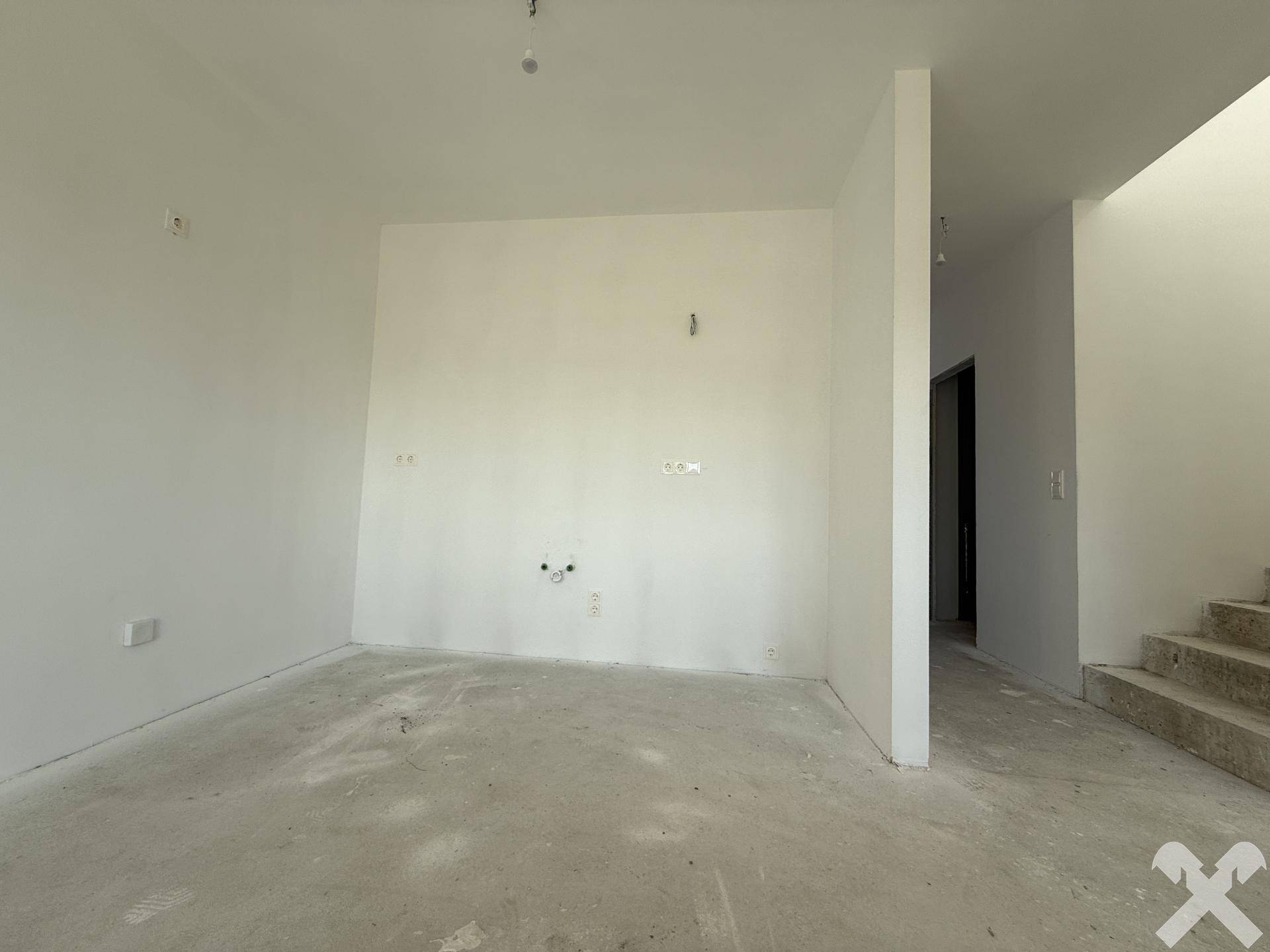 Geräumiger Wohnbereich im Rohbau mit weißen Wänden und vorbereiteten Anschlüssen.