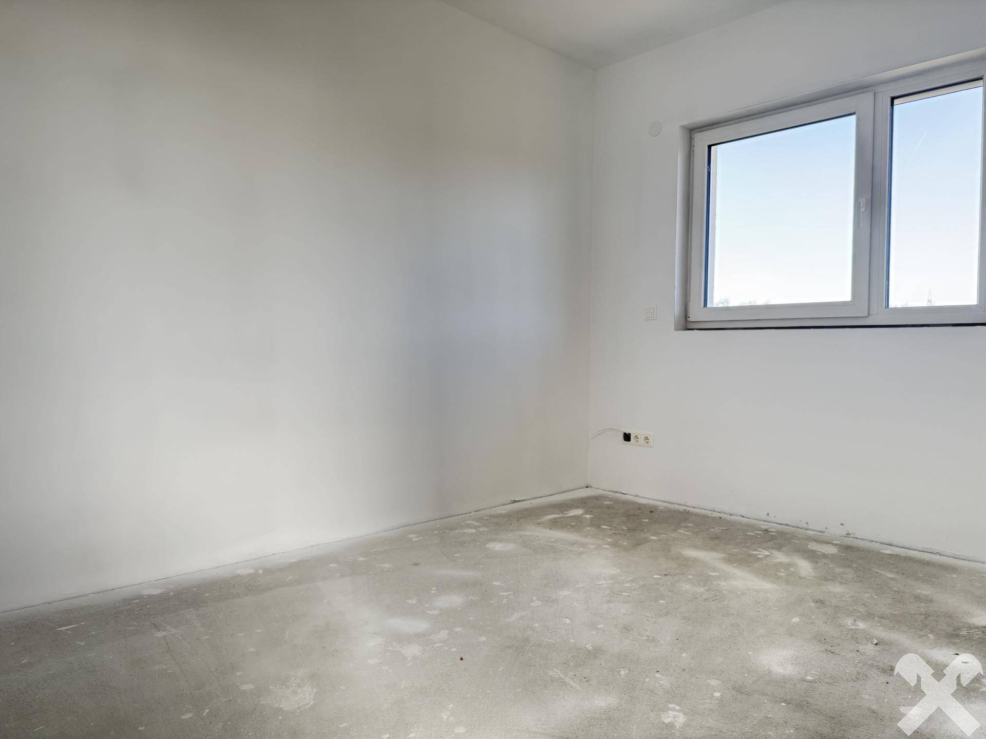 Helles Zimmer im Neubau mit Fenster und unfertigem Betonboden.