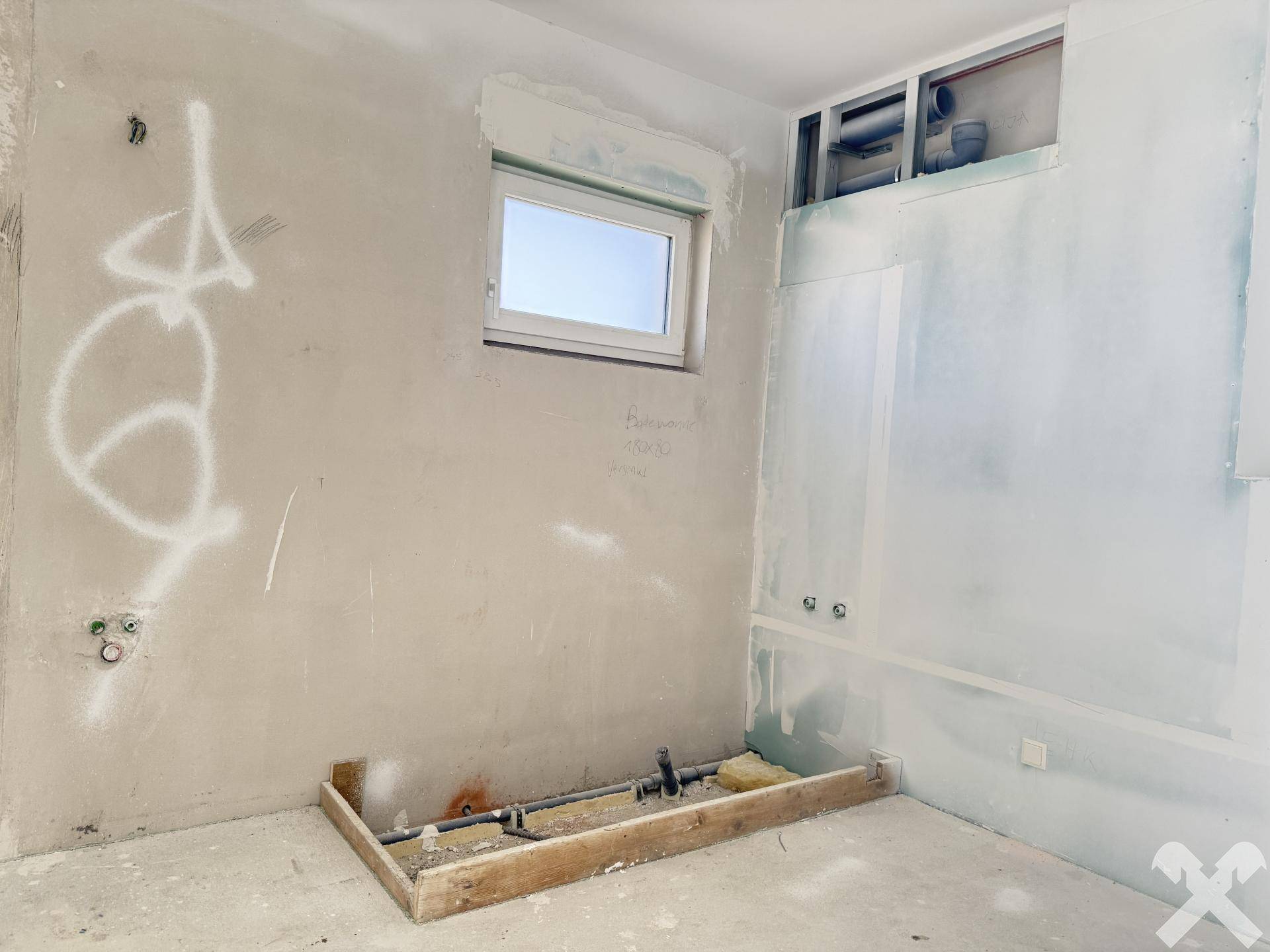 Badezimmer im Rohbau mit Fenster und vorbereiteten Installationen.