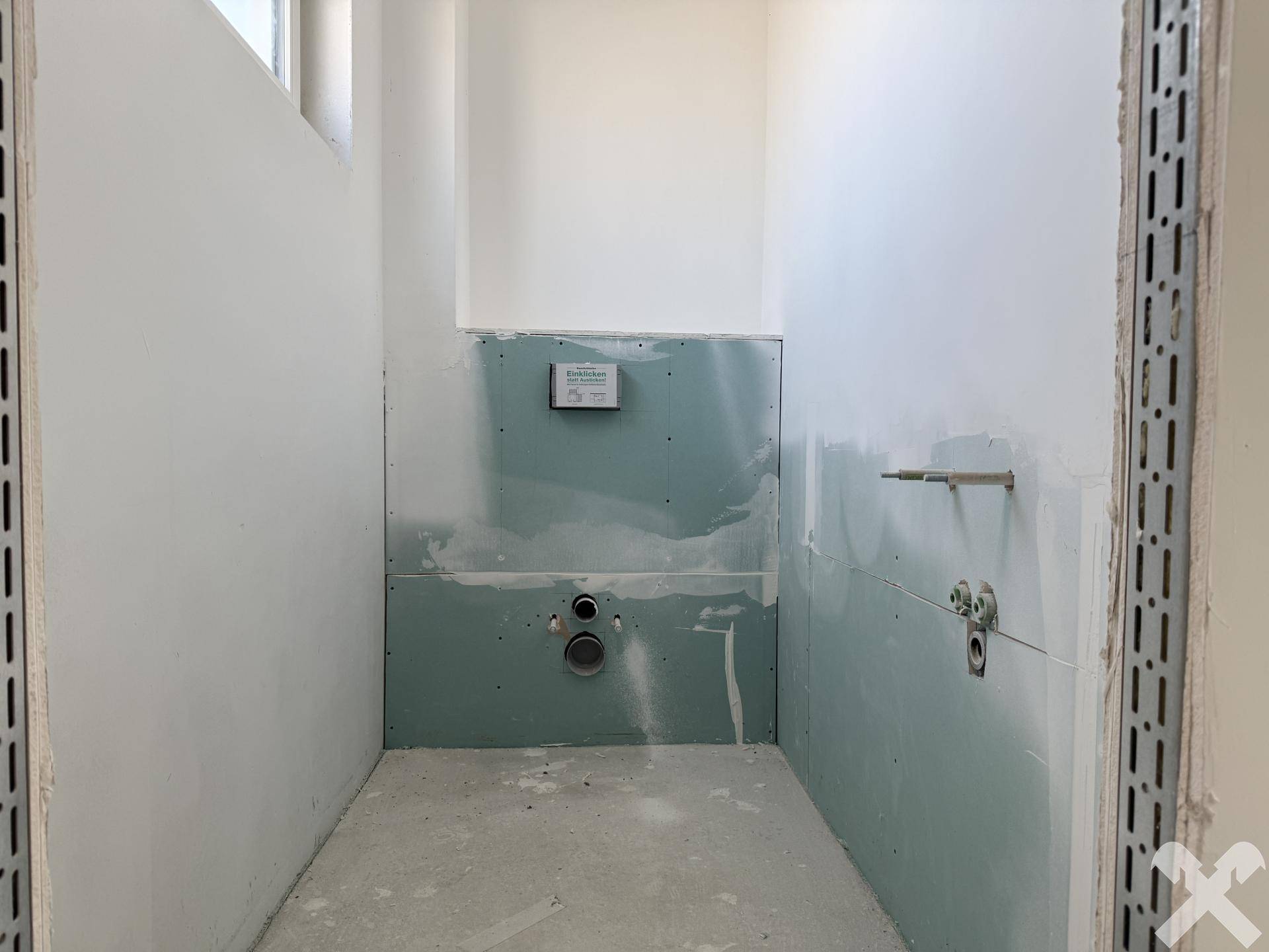 Badezimmer im Rohbau mit vorbereiteten Anschlüssen für Sanitärinstallationen.