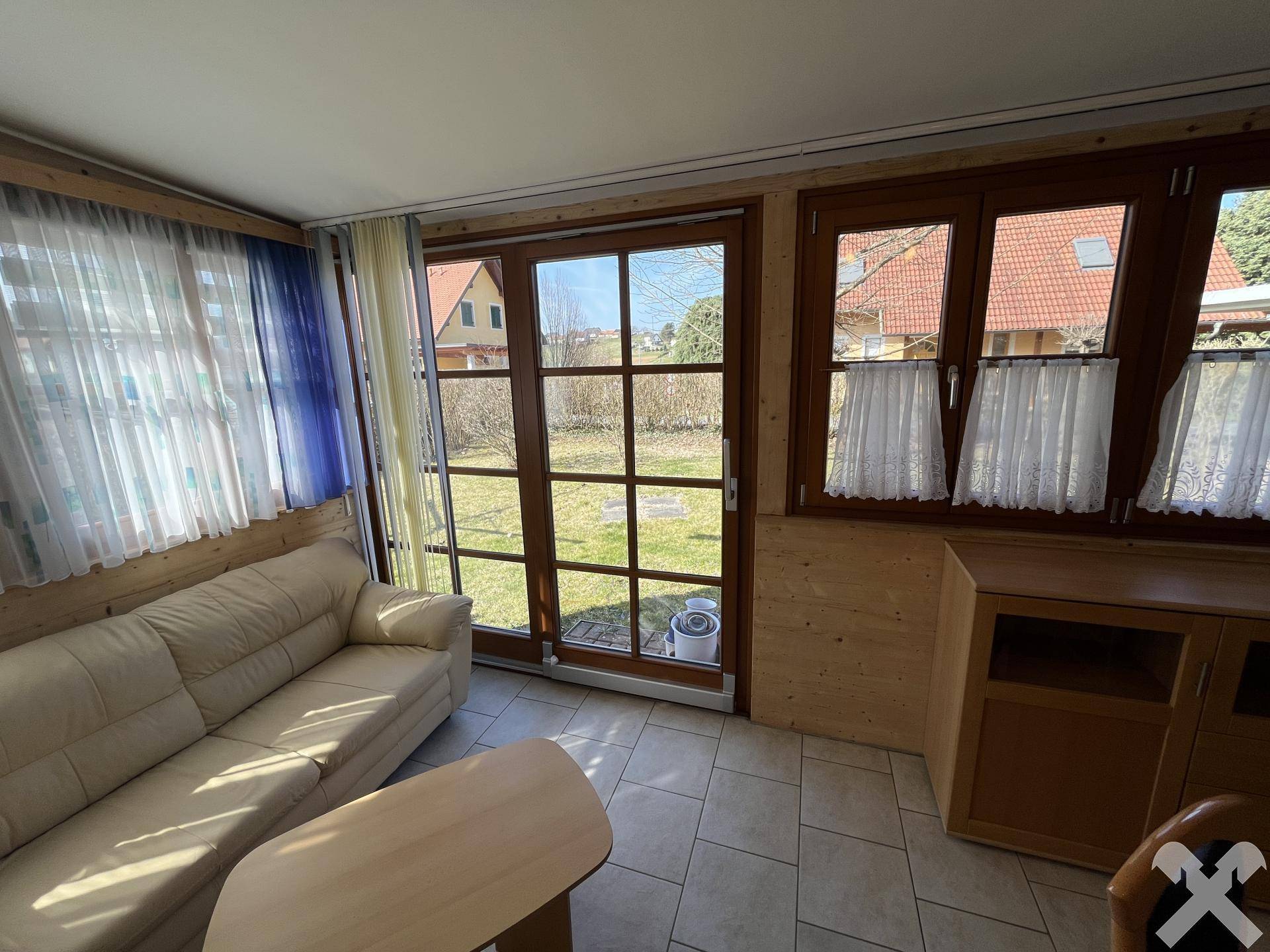Gemütlicher Wintergarten mit Sofa, Fliesenboden und großen Fenstern zum Garten.