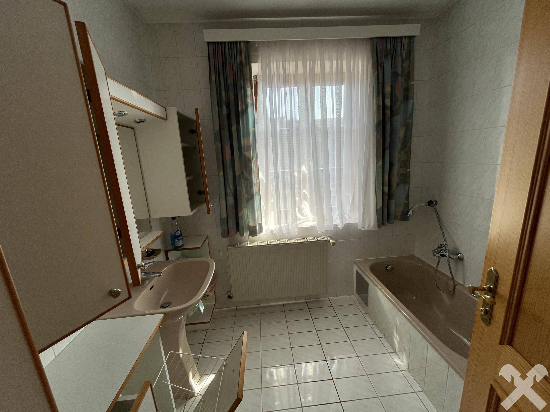 Badezimmer mit Fliesenboden, Badewanne, Waschbecken und Fenster.