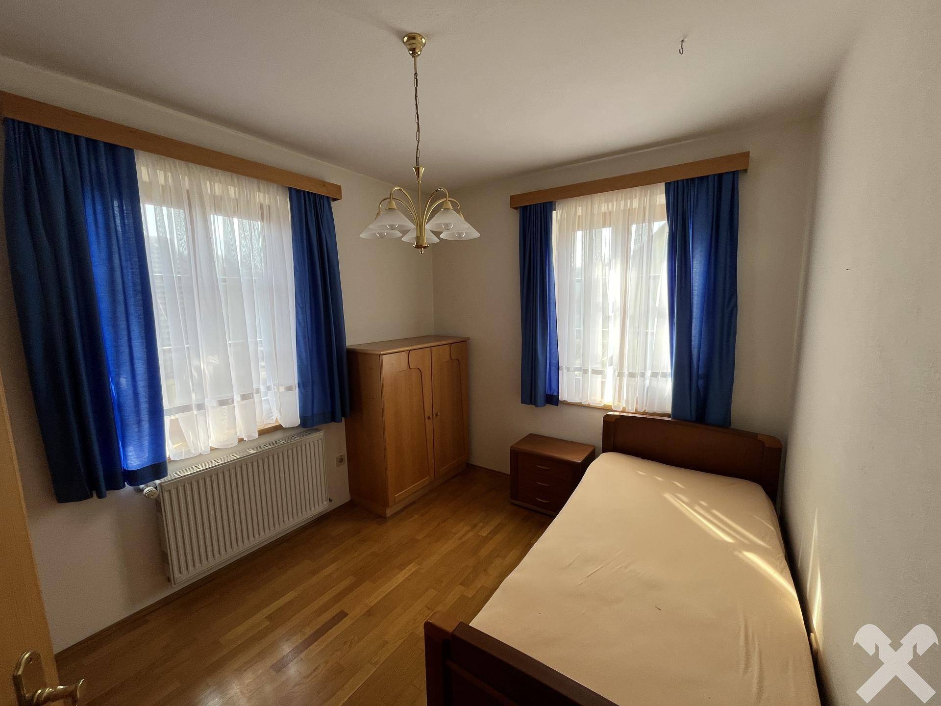 Helles Schlafzimmer mit Parkettboden, Einzelbett und blauen Vorhängen.