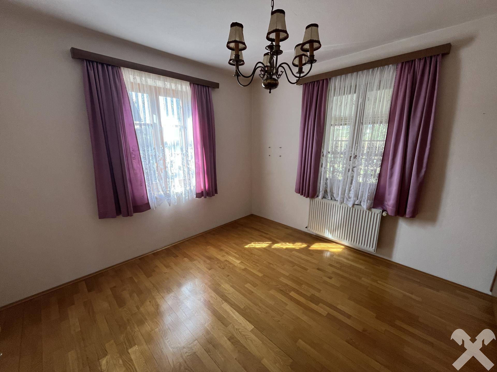 Schlafzimmer mit Parkettboden, zwei Fenstern und einem Kronleuchter.