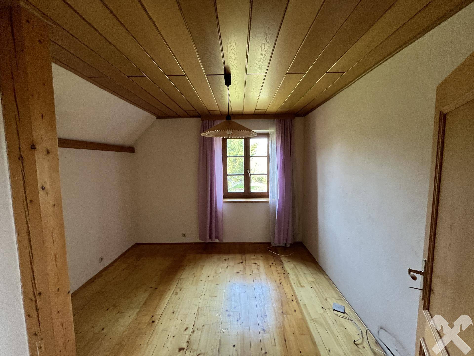 Gemütliches Dachzimmer mit Holzdecke, Parkettboden und Fenster.