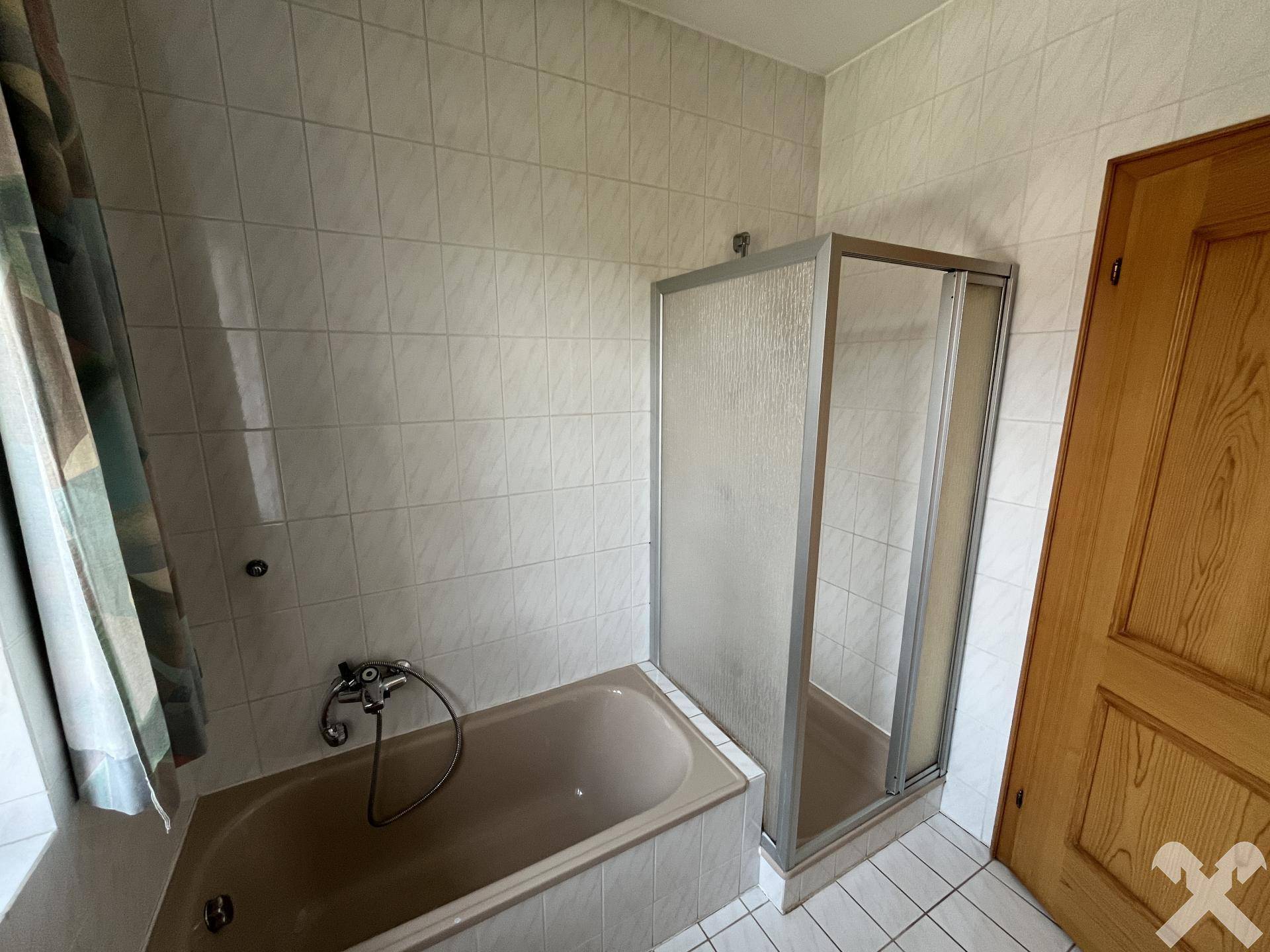 Badezimmer mit Badewanne, Duschkabine und Fliesen an Wänden und Boden.