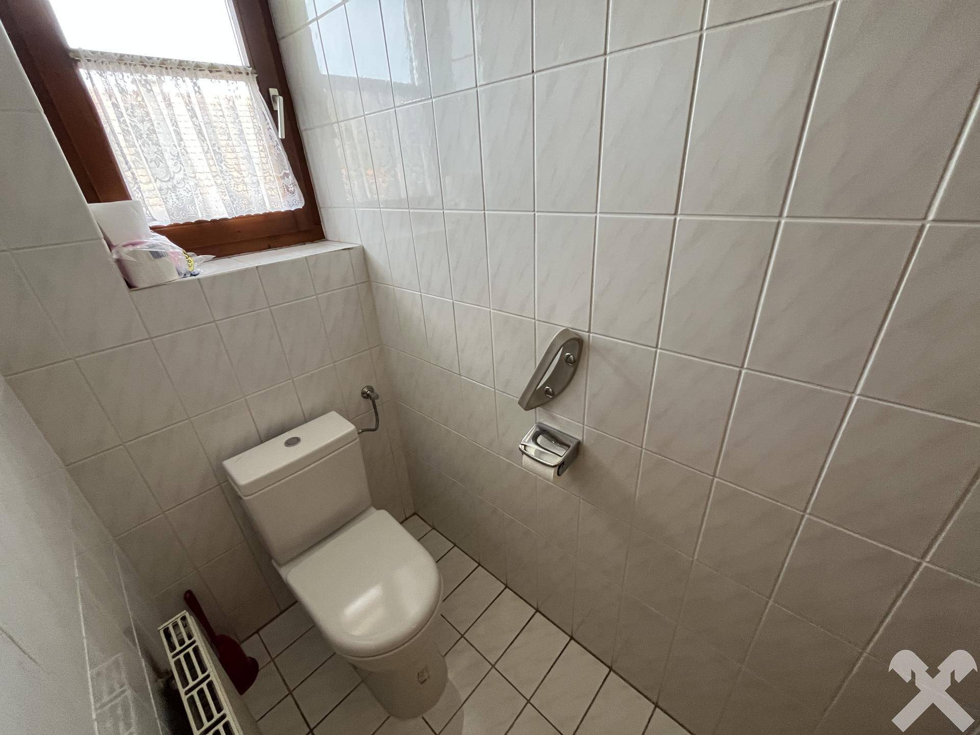 Separate Toilette mit Fliesenboden, WC und Fenster.