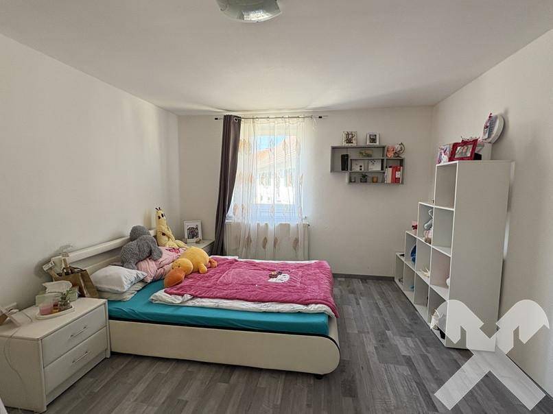 Kinderzimmer mit hellem Laminatboden, Einzelbett und weißem Regal für Spielzeug.