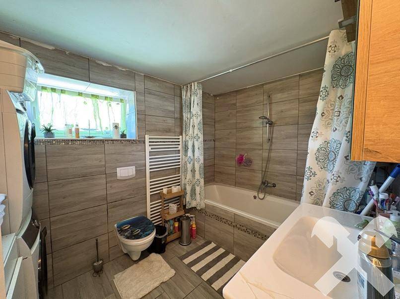 Badezimmer mit Badewanne, WC, Fliesenboden und Fenster für natürliche Belüftung.