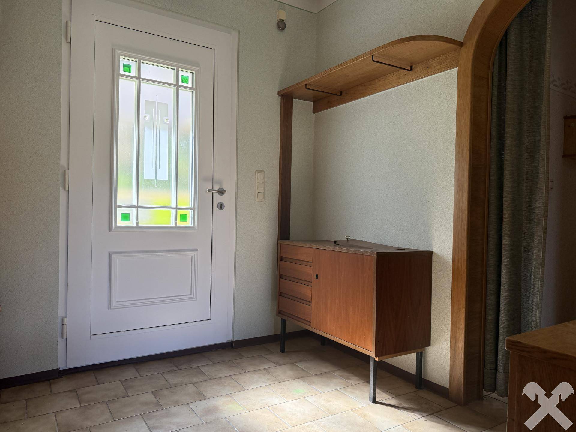 Eingangsbereich mit Fliesenboden, rustikalem Holzschrank und weißer Haustür mit Glaseinsätzen.