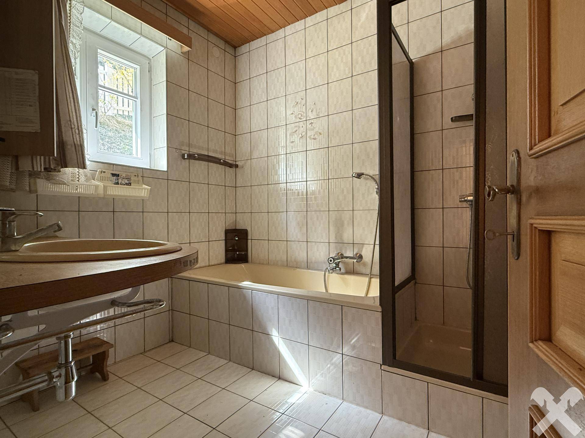 Badezimmer mit Badewanne, Duschkabine, Waschbecken und Fenster, gefliest in hellem Beige.