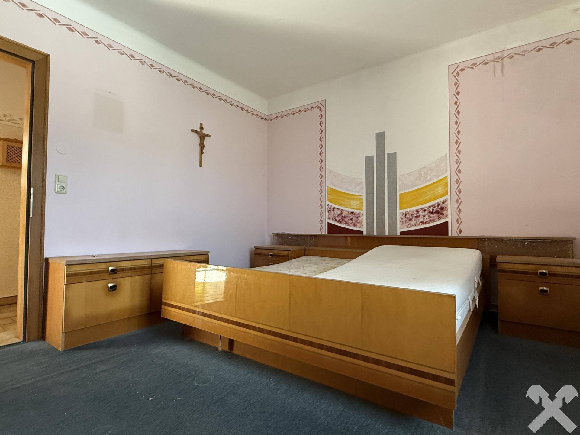 Schlafzimmer mit Doppelbett, Nachttischen und einfacher Wanddekoration in Pastellfarben.