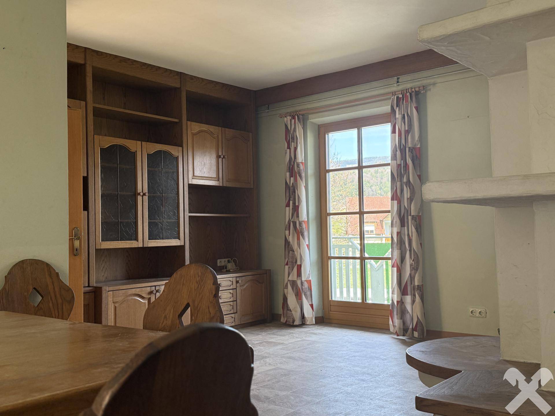 Wohnbereich mit Einbauschrank, Holztisch und Fenster mit Blick ins Grüne.