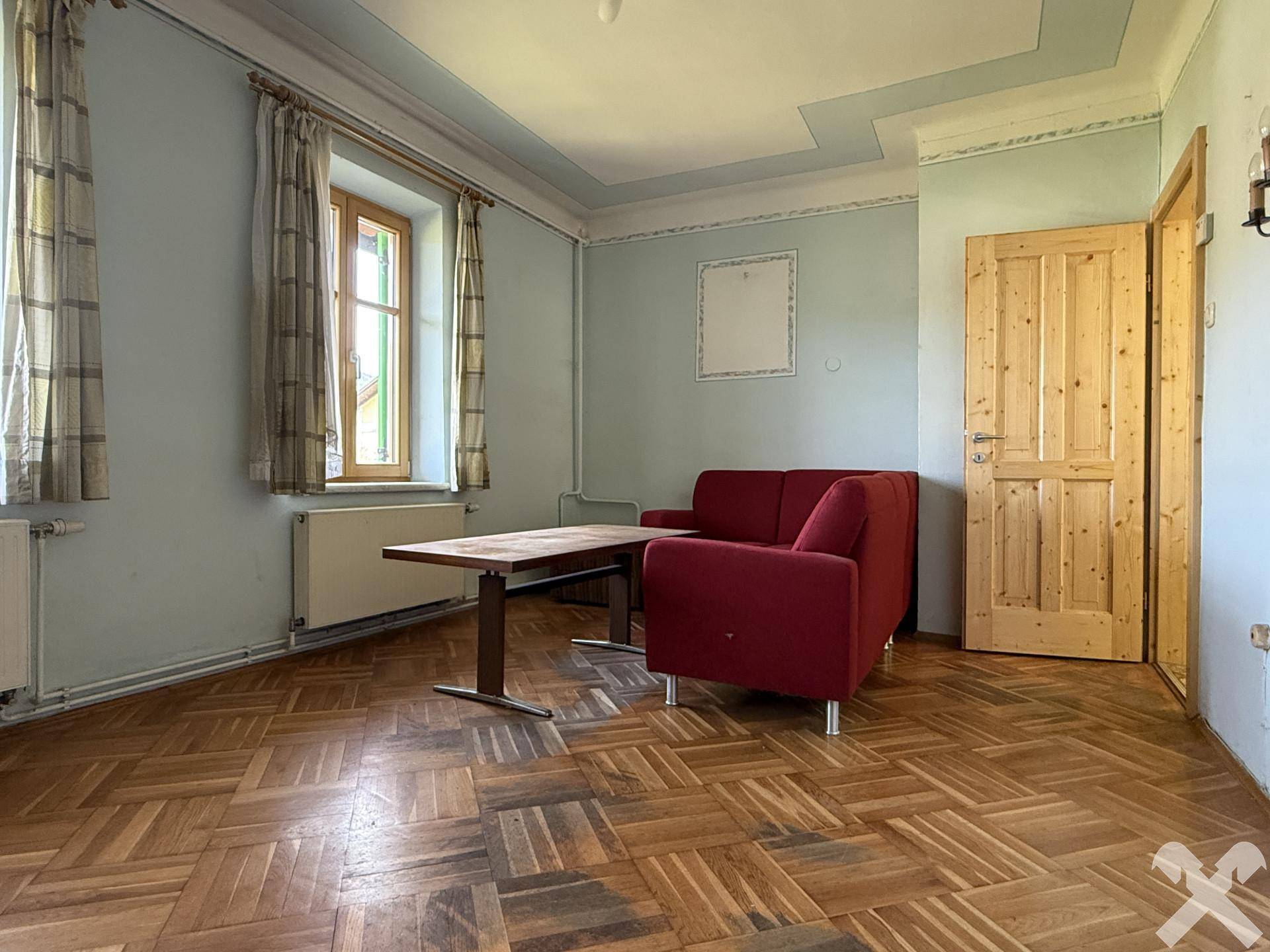 Wohnzimmer mit Fischgrätparkett, roten Sofas und hohen Decken, gut beleuchtet durch Fenster.