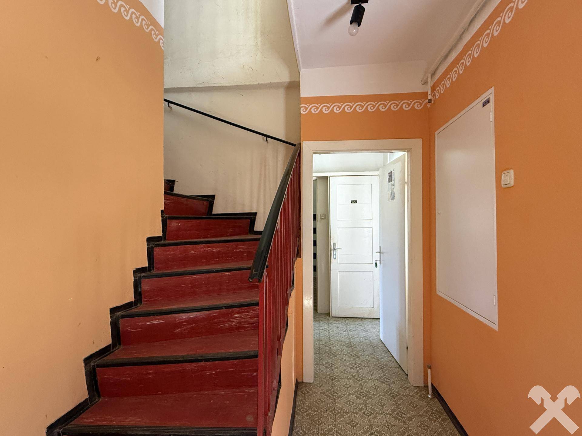 Treppenhaus mit roter Holztreppe und orangefarbenen Wänden, im Stil eines Altbaus.