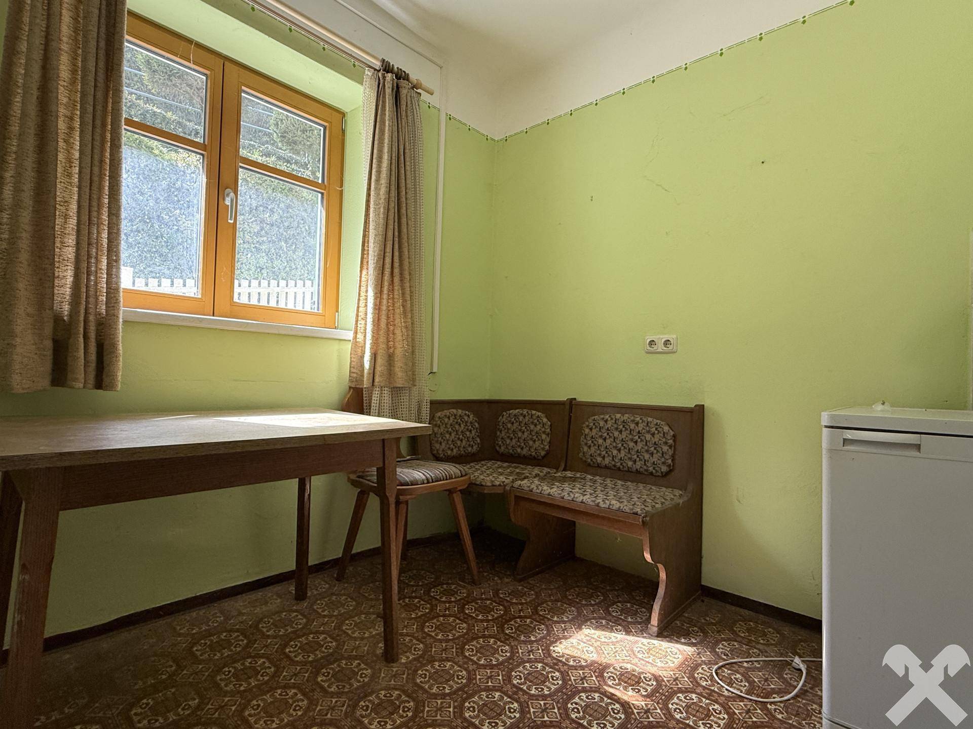 Kleine Küche mit Esstisch, Sitzbank und grünen Wänden, ausgestattet mit Kühlschrank.