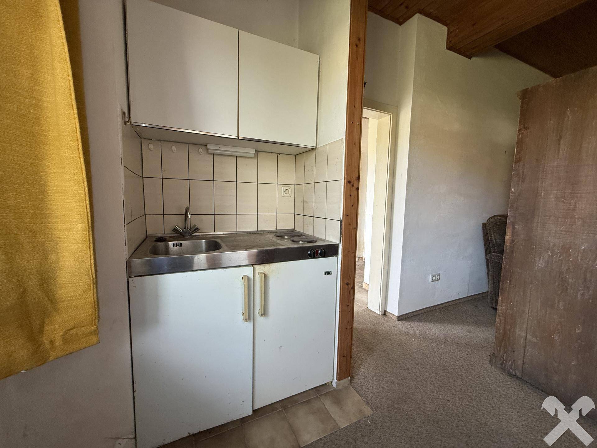 Kleine Küchenzeile mit Spüle und Kochfeld in einem Raum, ideal für eine Singlewohnung.